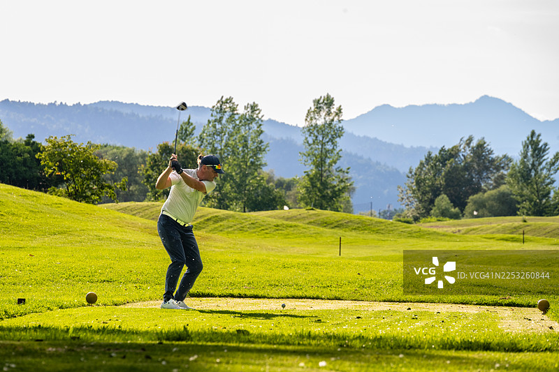 成熟的高加索男性在高尔夫球场的葱郁球道上挥杆图片素材