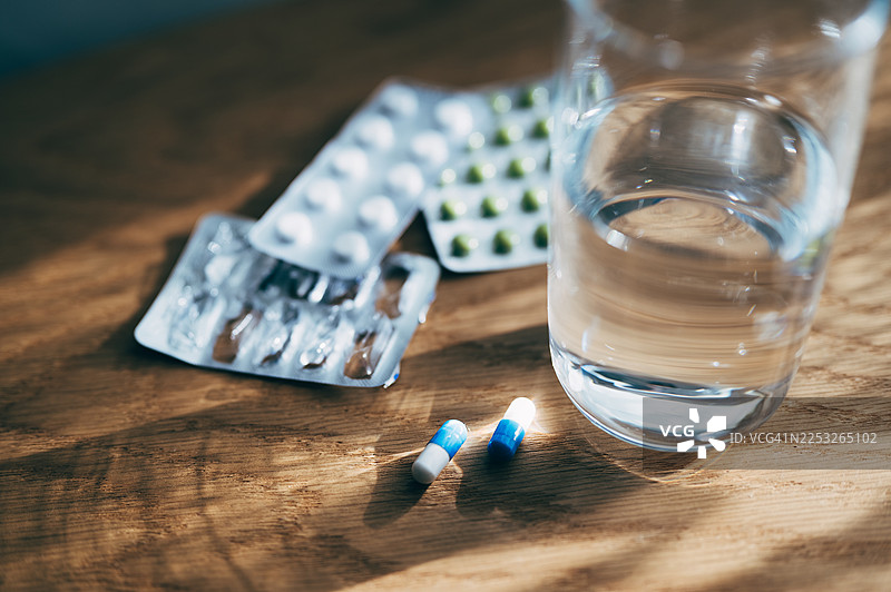 药片放在包装盒里，旁边还有一杯水放在桌子上图片素材