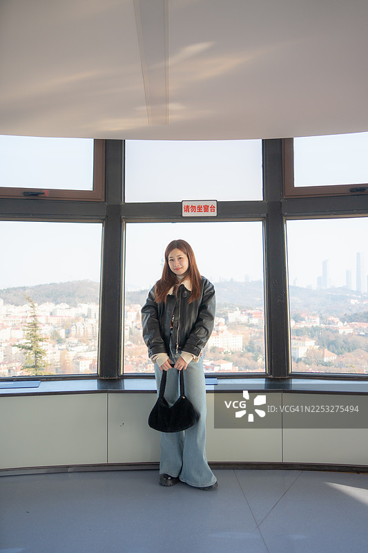 一位美丽的女士在青岛的山丘上漫步，远眺城市美景。图片素材