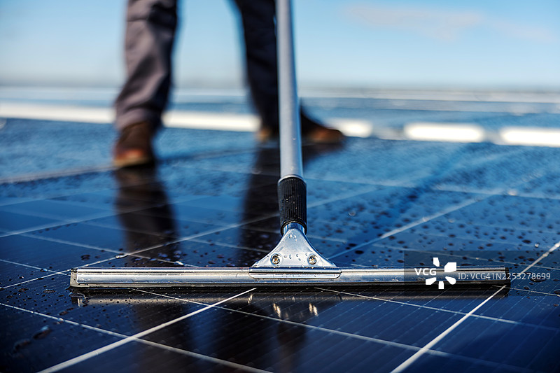 工人用刮水器清洁太阳能电池板进行维护图片素材