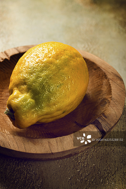 一个表面有纹理的鲜亮柠檬放在手工木盘上，在柔和的自然光下，温暖的厨房氛围衬托出其明亮的色彩图片素材