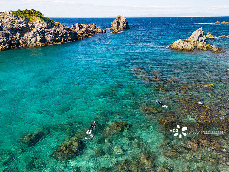从空中无人机镜头俯瞰式根岛（Shikinejima island），可以看到那珂浦海滩（Nakanoura beach），美丽湛蓝的海水和葱郁的森林，人们正在水面上游泳。图片素材