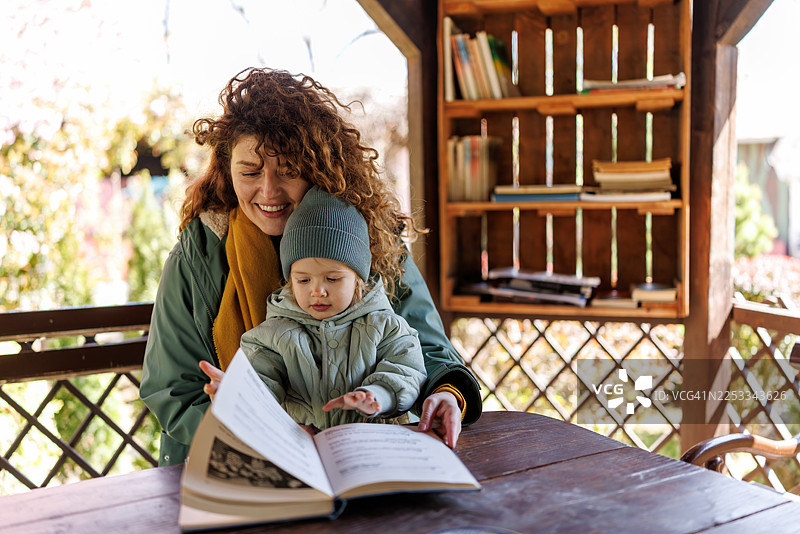 微笑的母亲和可爱的女儿在开放的图书馆里阅读儿童读物图片素材