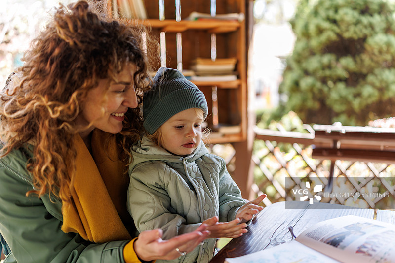 微笑的母亲和可爱的女儿在户外图书馆阅读儿童读物图片素材