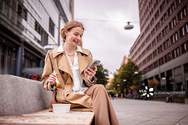 阴天，一位女士在柏林市中心的波茨坦广场一边使用手机一边享用零食图片素材