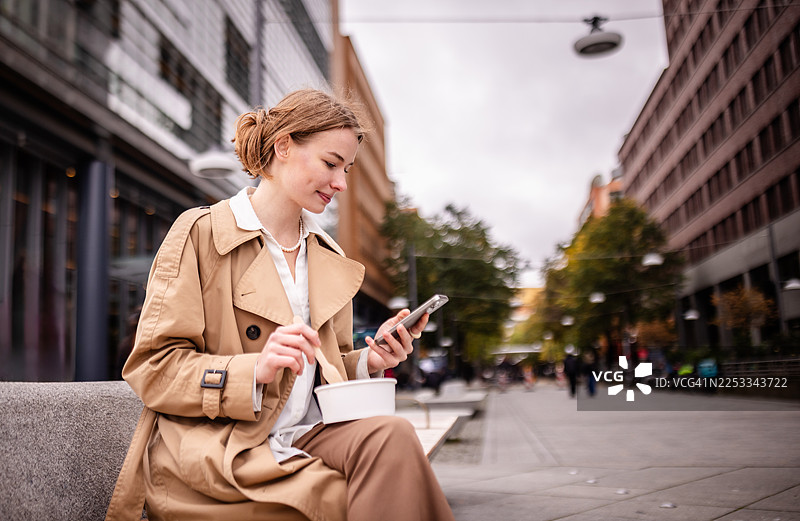 在城市繁忙的一天中，一位女士在柏林波茨坦广场边用餐边使用手机图片素材