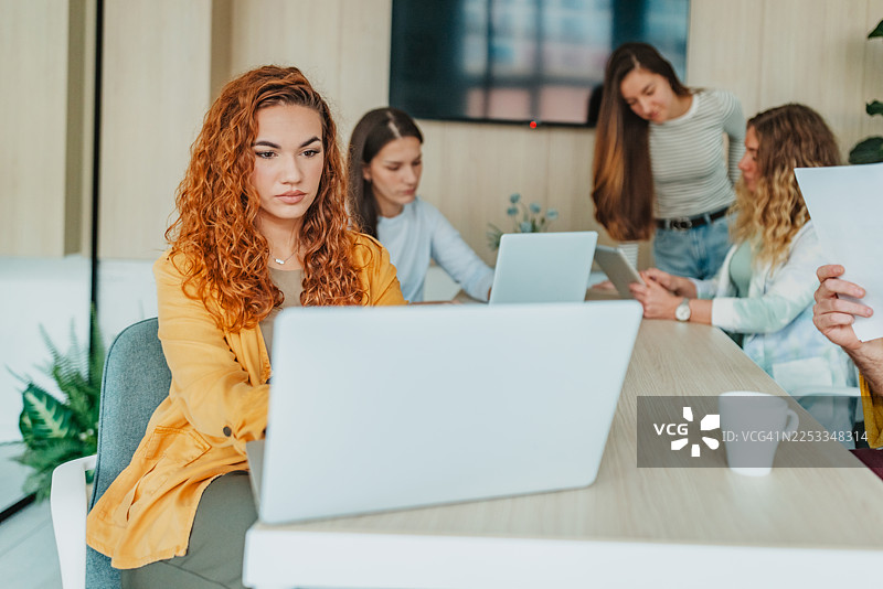 在工作时间内，一群成年人在办公室里使用笔记本电脑和文件进行协作工作。图片素材