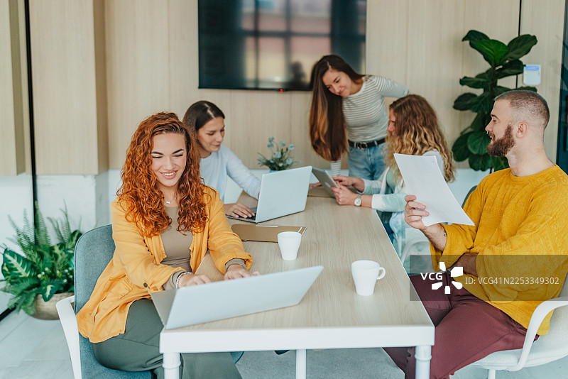 一群同事在白天于现代办公室空间里协作，使用笔记本电脑工作图片素材
