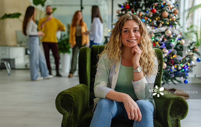 节日季，办公室里同事们正在交谈，一位女士坐在椅子上图片素材