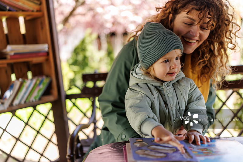 笑容满面的母亲和可爱的女儿在城市花园图书馆阅读儿童读物图片素材