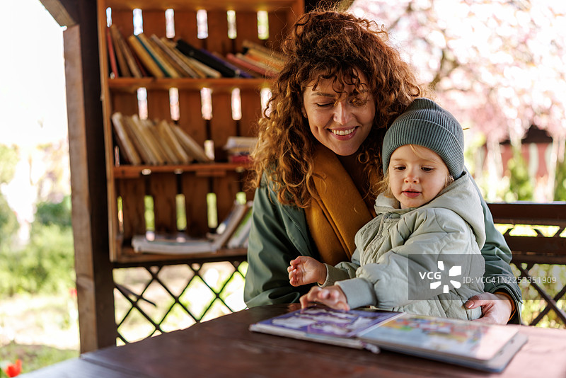 一位微笑的母亲和她可爱的女儿在城市花园图书馆里阅读儿童读物图片素材