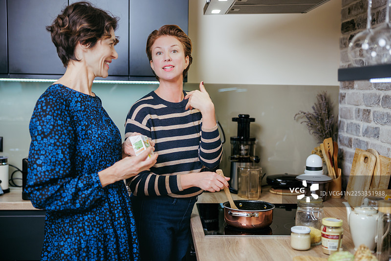 朋友在家做饭：两位女士在现代厨房里聊天并搅拌平底锅里的酱汁图片素材