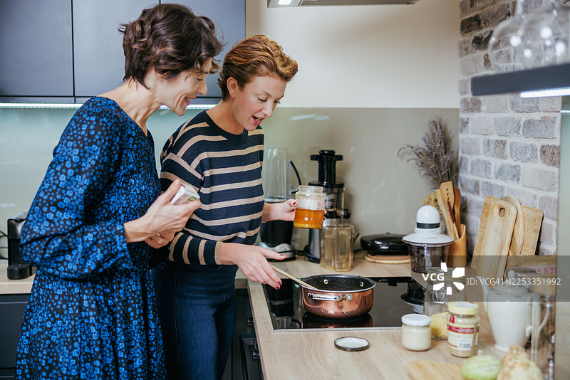 两位朋友在家中一同烹饪，在现代厨房里边笑着边开心地翻炒食物图片素材