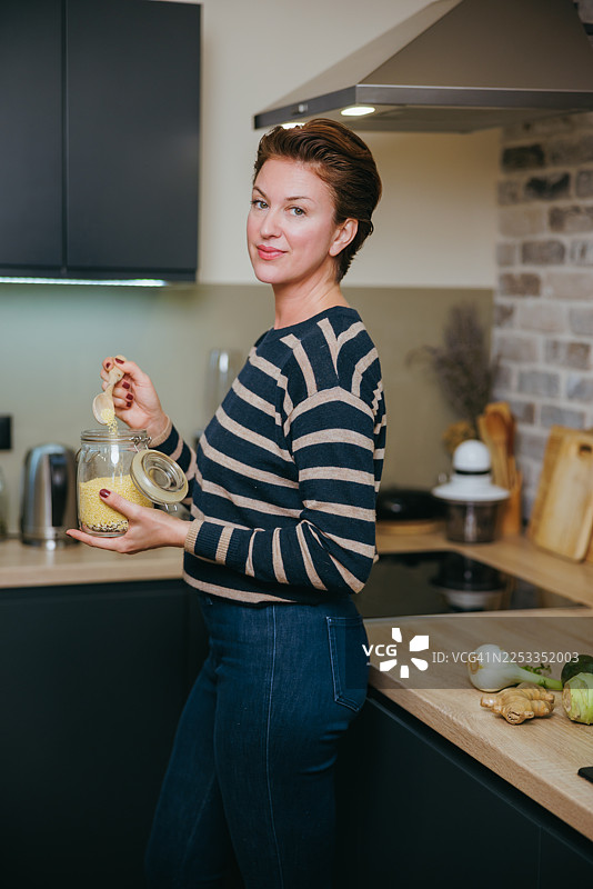 穿着条纹毛衣的女士在现代厨房里准备食材，开心地将谷物倒入罐中图片素材