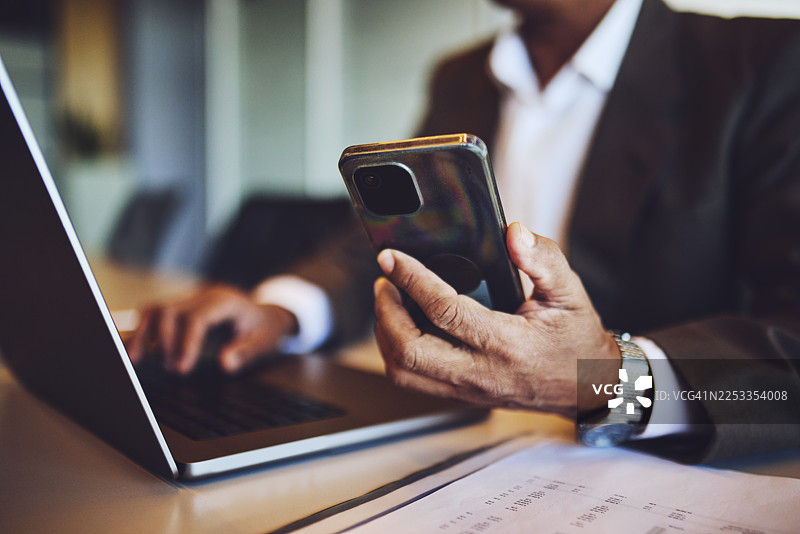 商务人士多任务处理：一边用智能手机一边在笔记本电脑上打字图片素材