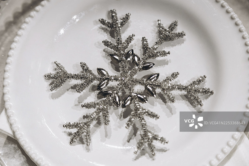 一个银色的雪花装饰品，优雅地摆放在一个纯白色的陶瓷盘子上。图片素材