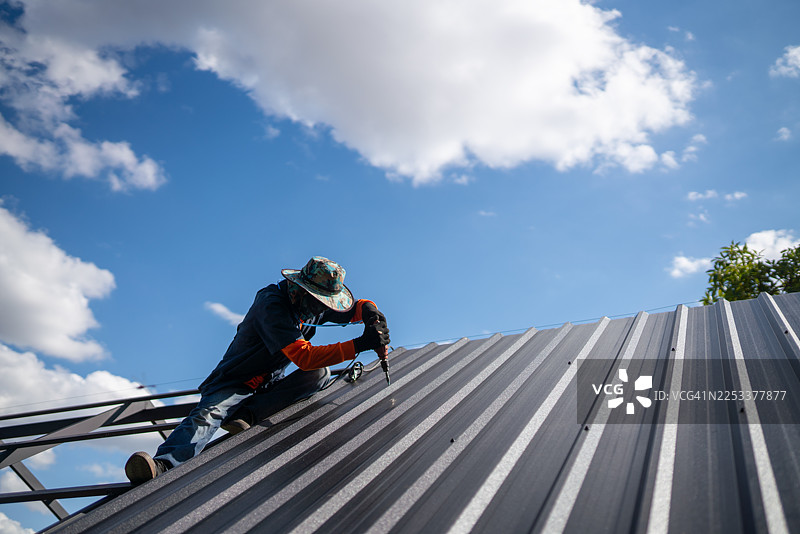 工人正在建筑工地上安装金属屋面板，户外仰拍，熟练的劳动力正在工作中图片素材