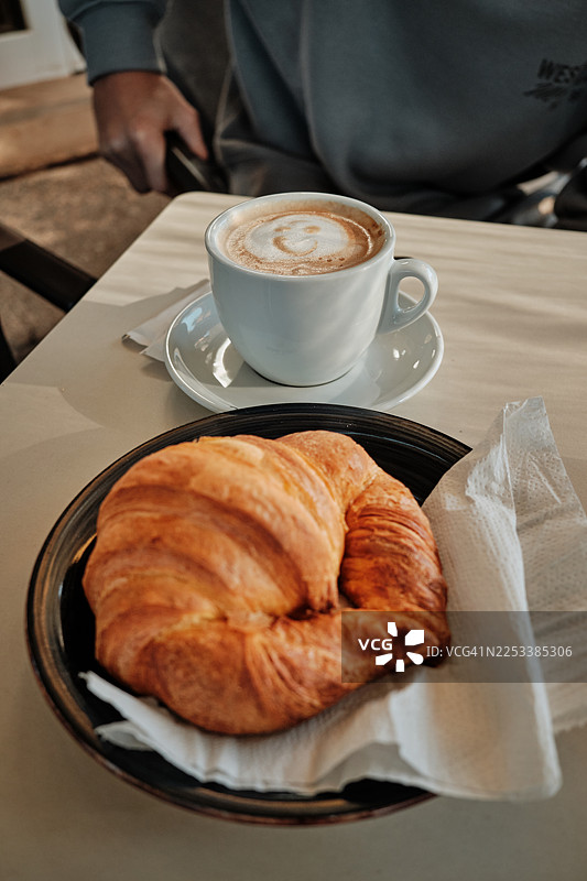 桌上的牛角包和带有拉花艺术的卡布奇诺咖啡图片素材