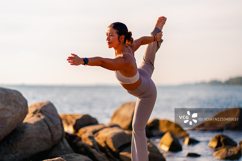 女子在自然海岸环境中全神贯注地掌握高难度瑜伽体式的动态户外肖像。图片素材