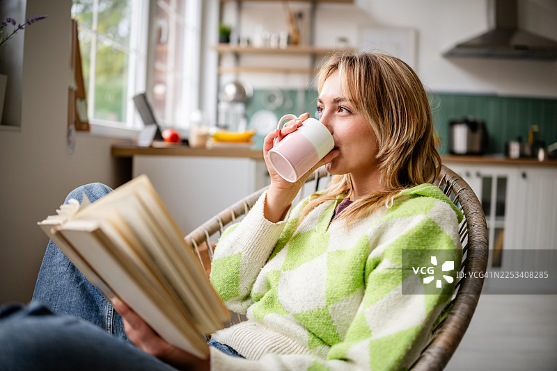 年轻女子在舒适的厨房里，公寓里放松地阅读书籍，啜饮咖啡。图片素材