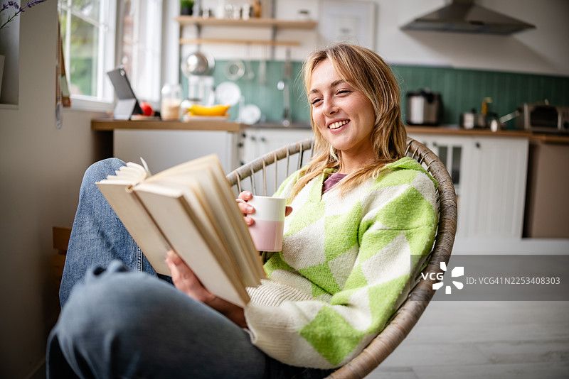 年轻女子在明亮的厨房里享受早晨的阅读时光，品尝着茶图片素材