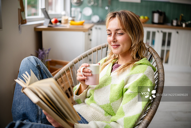 年轻女子在家中放松时刻，一边喝着咖啡一边在厨房阅读图片素材