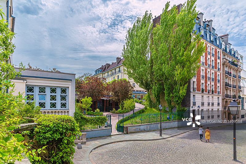 法国一座欧洲城市的迷人鹅卵石街道，历史建筑和茂密的绿树在多云的天空下图片素材