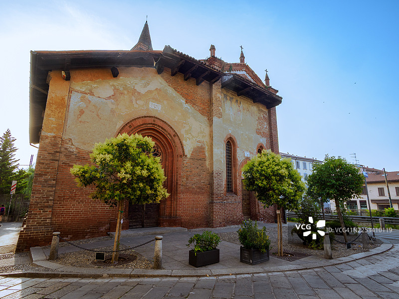 一座拥有独特尖塔的历史悠久的教堂，在晴朗的蓝天下，绿树和鹅卵石街道环绕，米兰，意大利，圣克里斯托福罗苏纳维廖。图片素材
