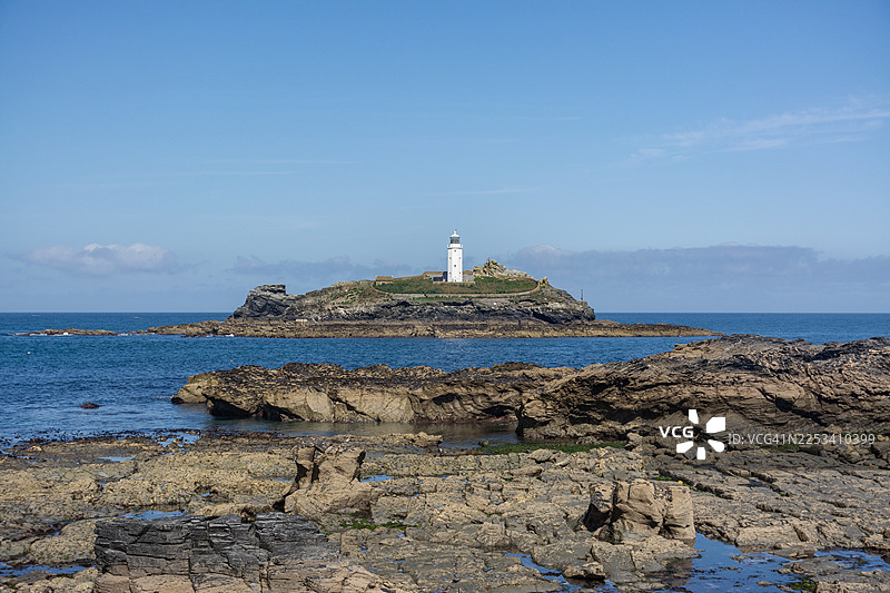 英国戈德雷灯塔，岩石岛上的白色灯塔，崎岖的海岸线和蓝色的海洋，在晴朗的天空下，英国，英国图片素材