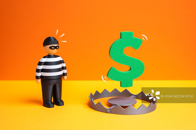 一个强盗玩偶站在带有美元符号诱饵的钱箱旁，象征着财务风险和欺诈图片素材