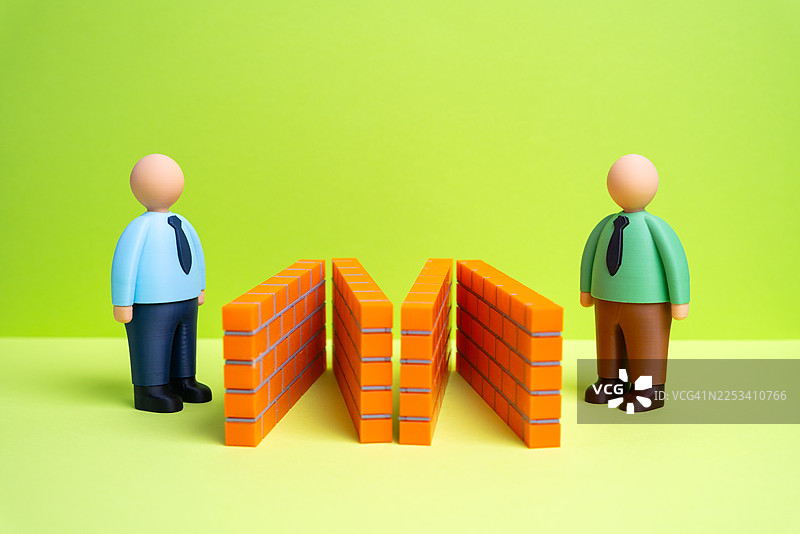 两个玩偶人被砖墙隔开，背景为绿色，象征着分离和沟通障碍的概念图片素材