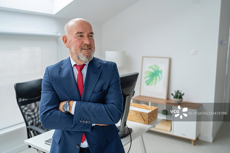 自信的企业家肖像，他双臂交叉，面带微笑，站在现代办公室里图片素材