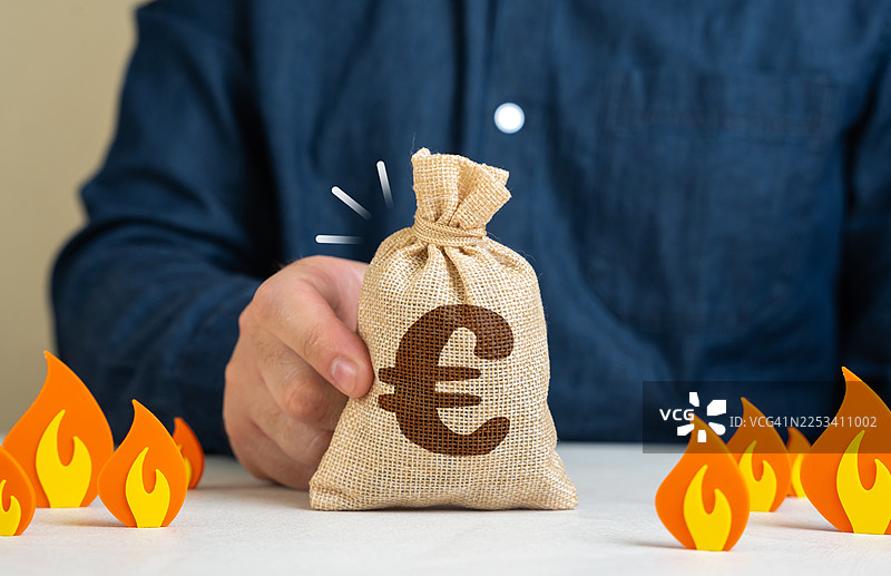 一个人拿着一个欧元符号的钱袋，周围环绕着装饰性的火焰，象征着金融风险或危机图片素材
