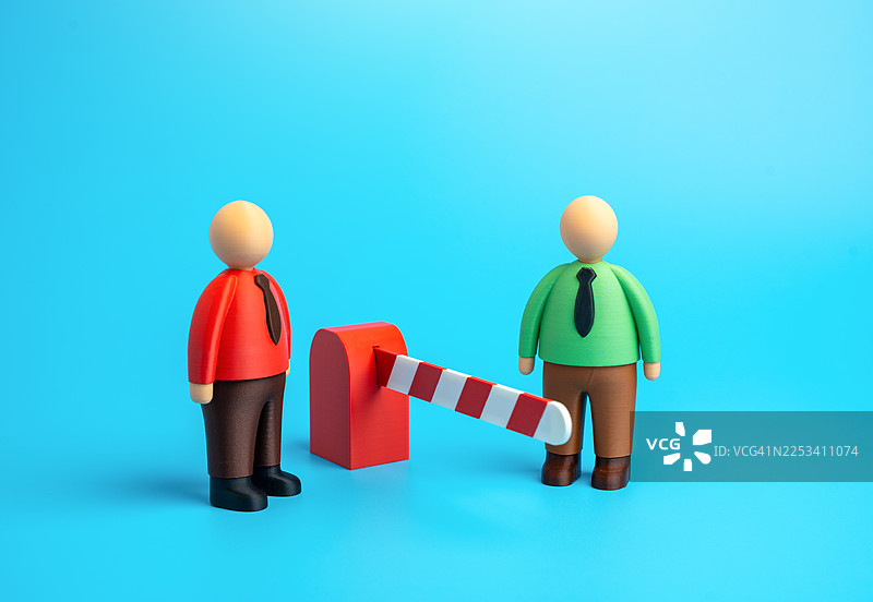 两个玩偶人站在放下的障碍物两侧，象征着限制或封闭的道路图片素材