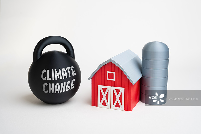 写有“气候变化”字样的壶铃，旁边是红色的小谷仓和粮仓，象征着环境问题对农业和农村生活的影响图片素材