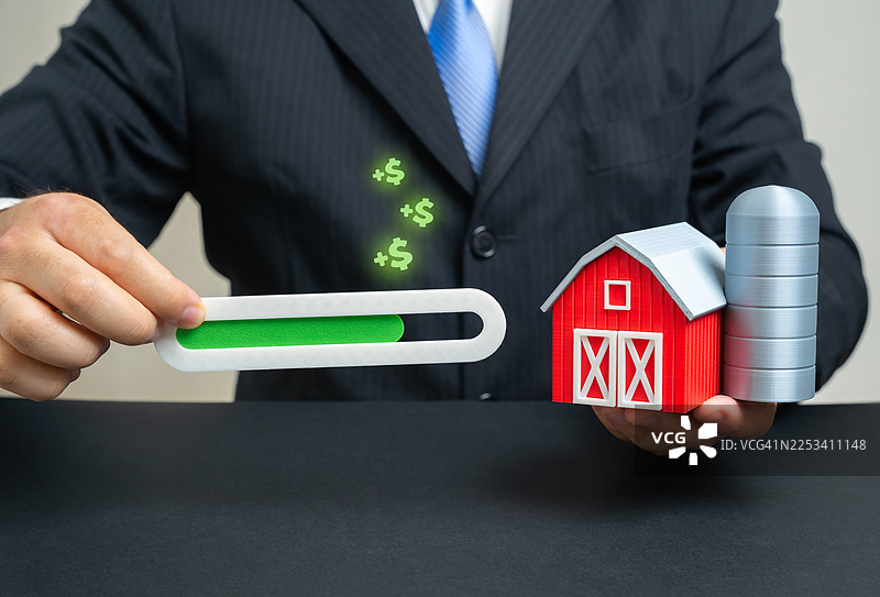 一名商人手持带有粮仓和绿色进度条的农舍模型，象征着农业的增长与投资图片素材