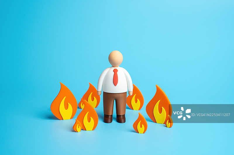一个商人玩偶被纸火焰包围，背景为蓝色，象征着压力和问题图片素材