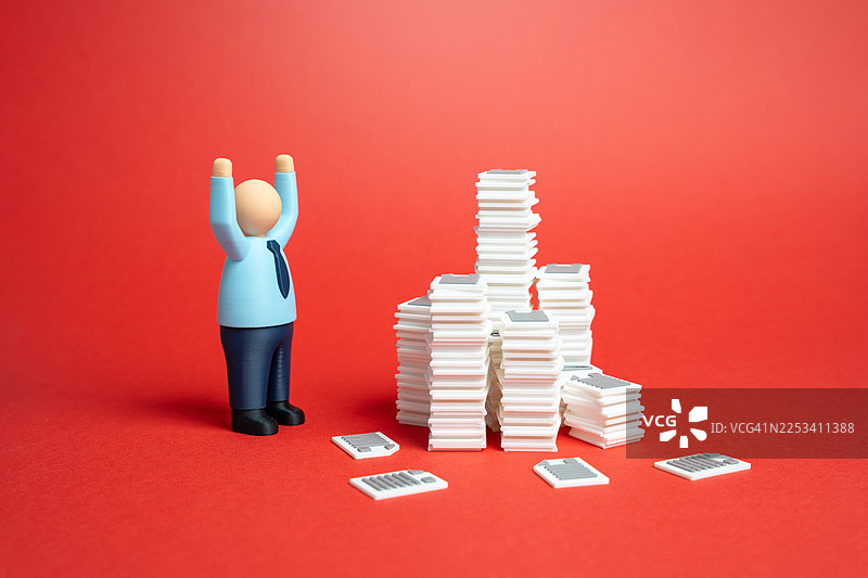 一个举着手的男性人偶站在文件堆旁边，象征着商业上的成功与成就图片素材