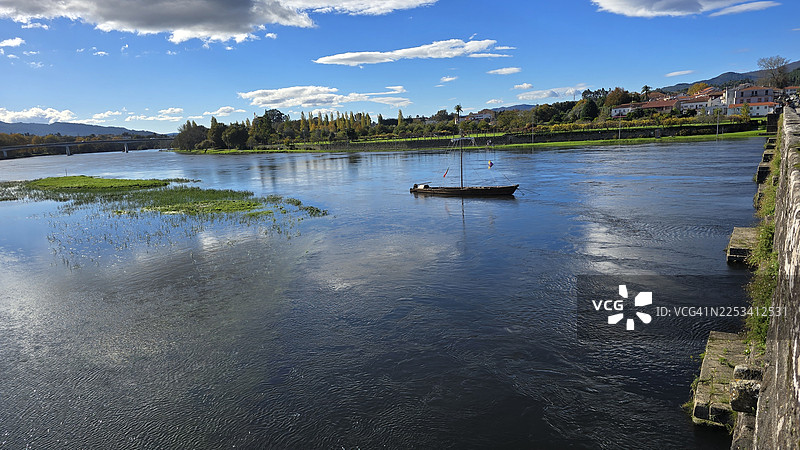 宁静河流的风景，有小船，两岸绿意盎然，远处有城镇，天空湛蓝图片素材
