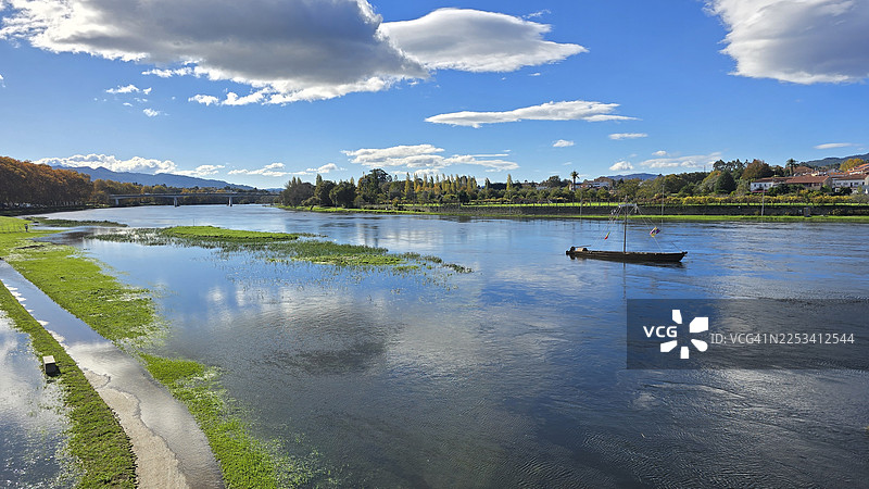 在蓝天白云下，宁静的河流上漂着一艘传统小船，构成一幅风景画图片素材
