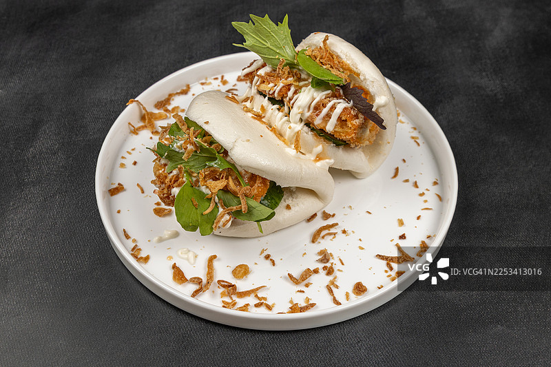 白色盘子里的美味包子，配有酥脆的炸料和新鲜蔬菜，背景为深色，准备食用图片素材