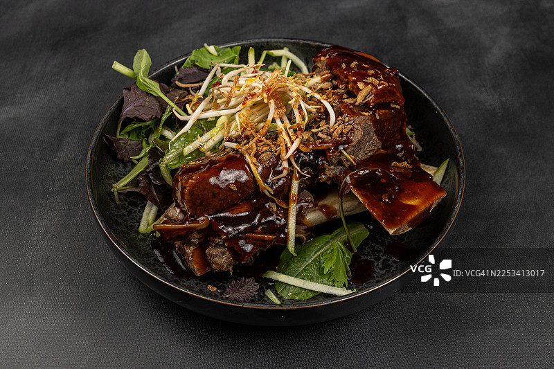 黑色背景下，深色碗中盛放着美味的炖排骨、新鲜沙拉和豆芽，俯视角度拍摄图片素材