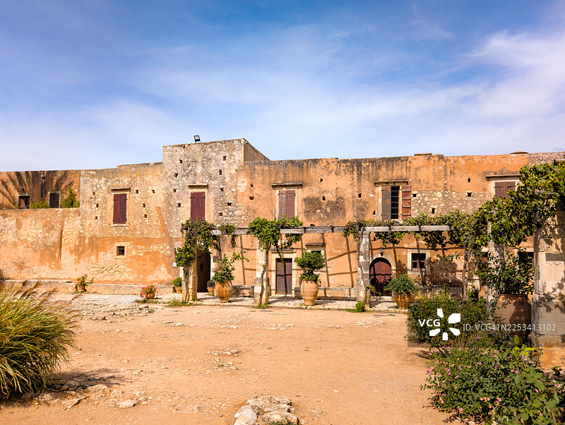 希腊克里特岛历史悠久的Arkadi威尼斯修道院，拥有传统建筑和郁郁葱葱的绿植，背景是晴朗的蓝天图片素材