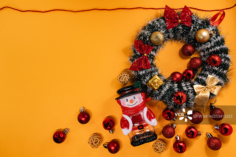充满活力的圣诞装饰，包括一个节日花环、雪人摆件和红色装饰球，摆放在明亮的橙色背景上，营造出欢乐的节日氛围图片素材