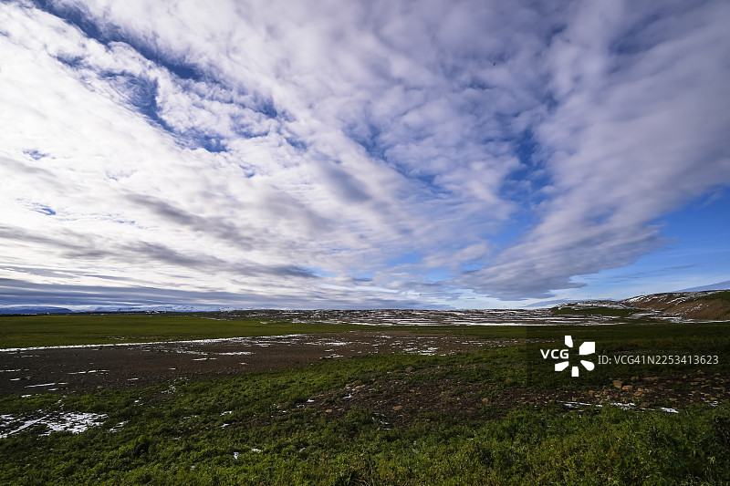 冰岛，广阔的绿色和棕色田野，点缀着雪斑，天空乌云密布，景色壮丽图片素材