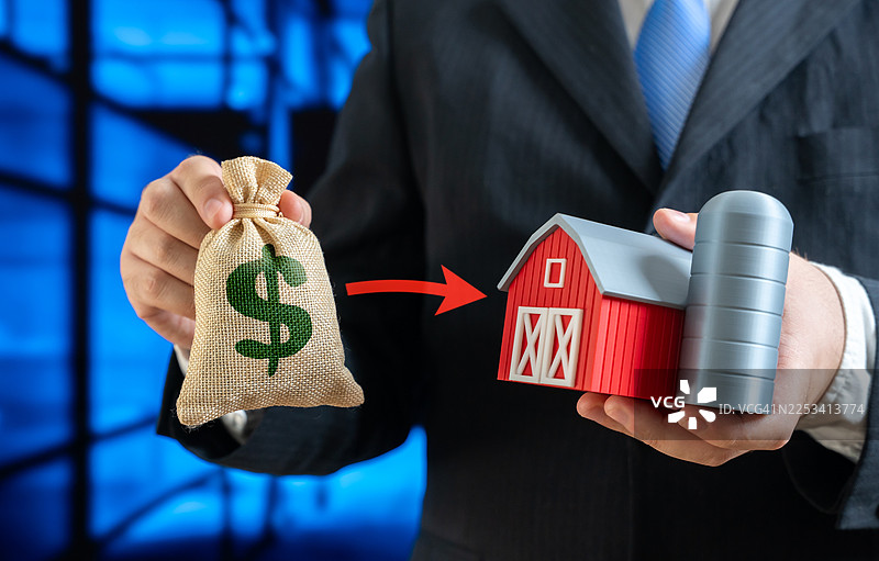 商人手持钱袋和农场模型，象征着对农业或农村地产的投资图片素材