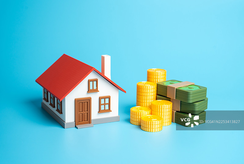 带有红色屋顶的样板房和堆积的钱，背景为蓝色，象征房地产投资和金融图片素材