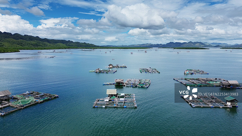 高角度视角，广阔大海中的传统渔船和养鱼场，下方是郁郁葱葱的绿色山脉，天空布满云彩图片素材