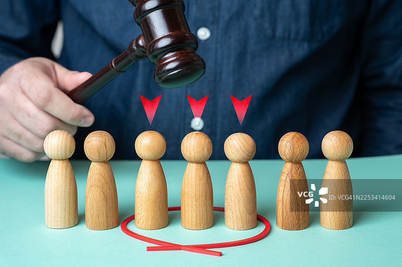 一只手举着法槌，指向一排木制小人偶，其中一些被红圈和箭头标出，象征着法律裁决或选择图片素材
