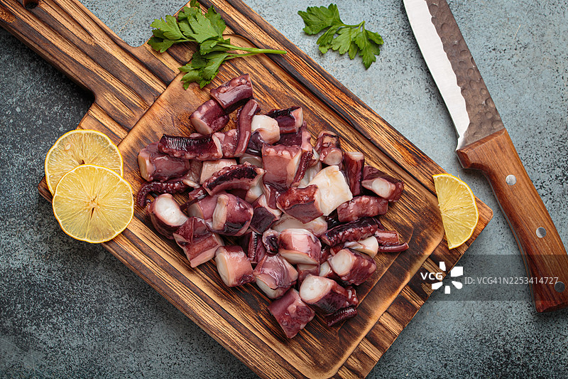 俯视角度拍摄的章鱼触手和柠檬片，放在带有刀具的质朴木质砧板上图片素材